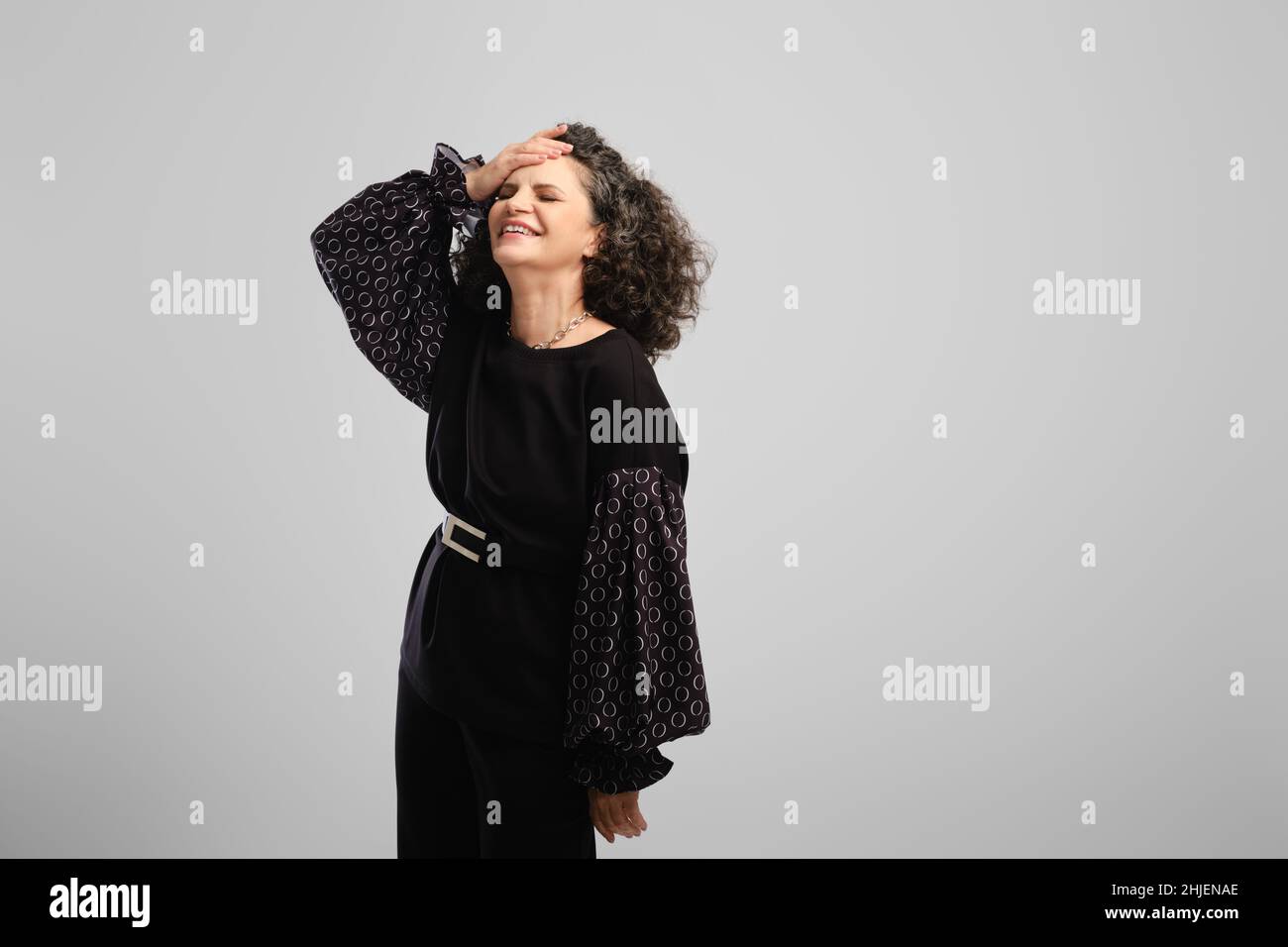 Very happy senior woman with lush curly hair laughing in studio over grey background Stock Photo