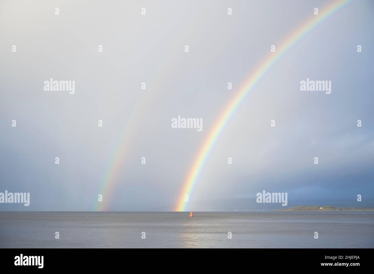 Bright rainbow high in sky over sea during dark storm Stock Photo