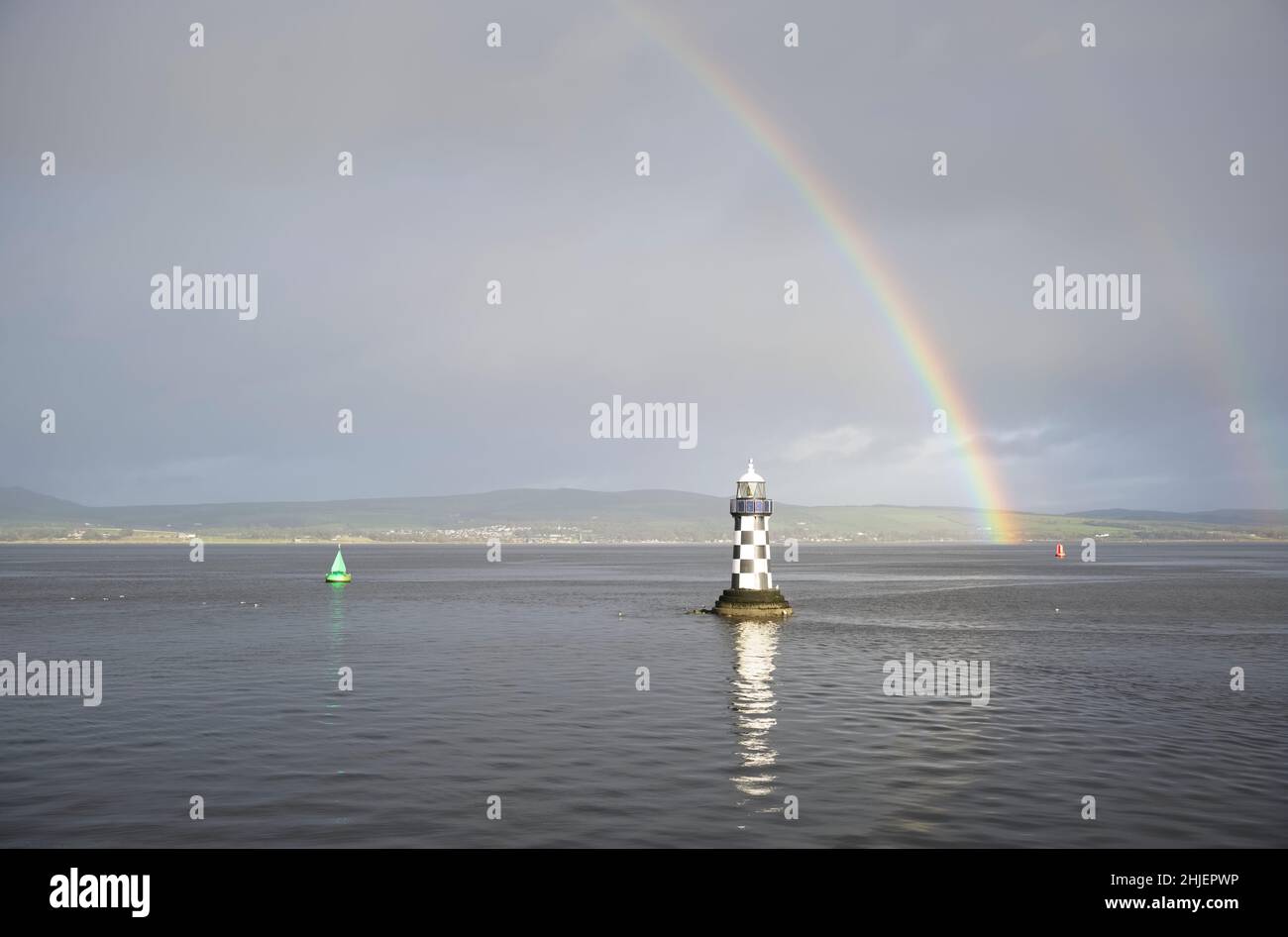 Bright rainbow high in sky over lighthouse in sea during dark storm Stock Photo