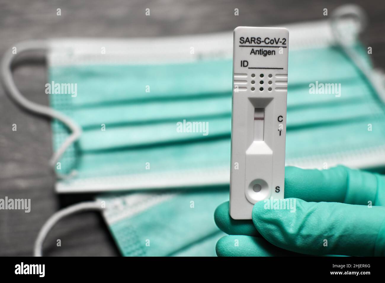 Hand with disposable glove holds coronavirus test kit with face masks in the background. Rapid antigen self-test shows negative result Stock Photo
