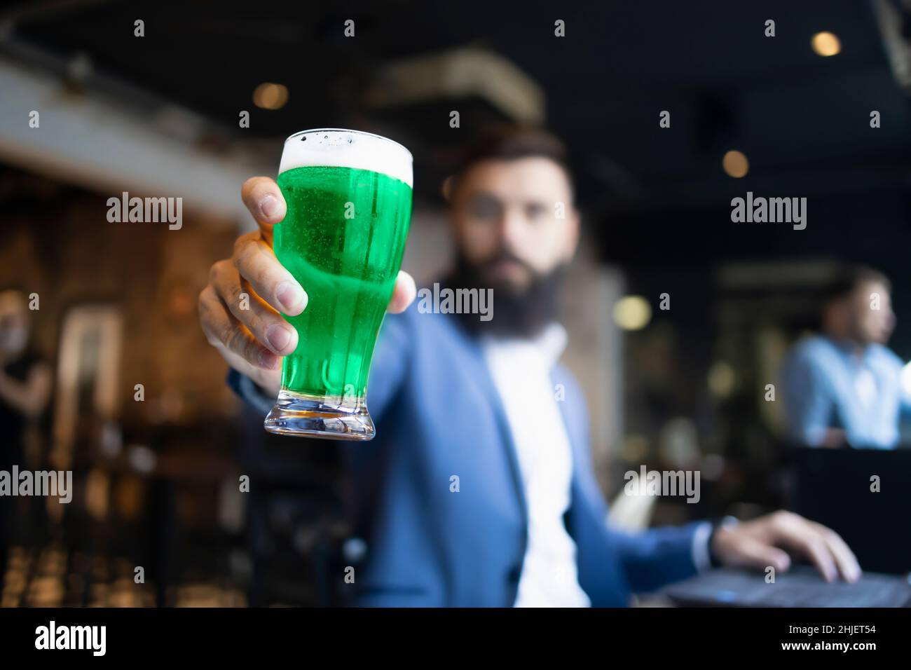 A man holding green glass of beer in a pub during St. Patrick's Day Stock Photo