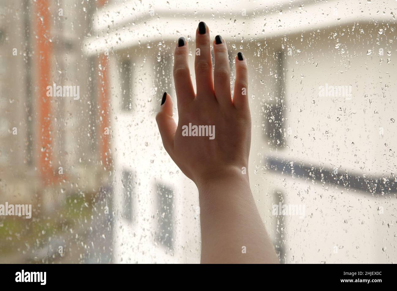 Hand of young girl touches window glass, outside rainy cold weather, urban area Stock Photo