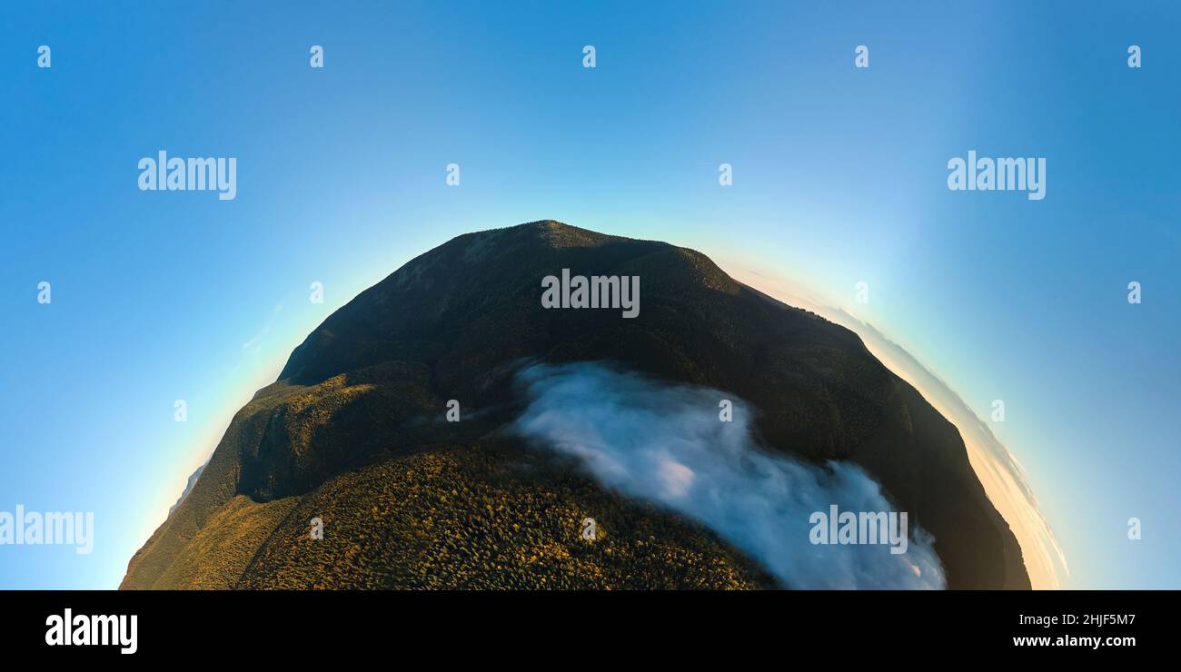 Aerial view from high altitude of little planet earth at sunrise covered with evergreen forest and high mountain peaks. Stock Photo
