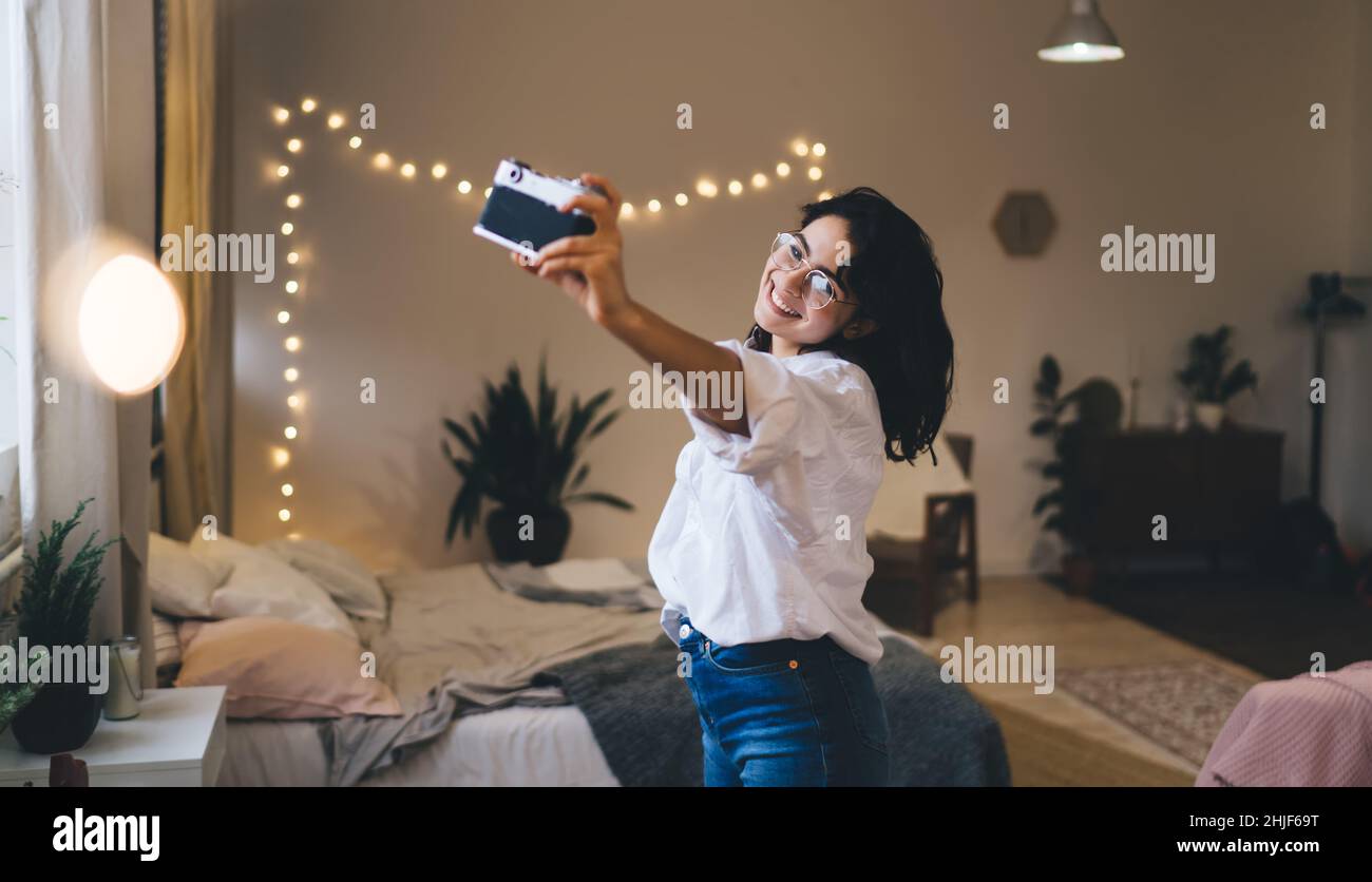 Smiling woman taking selfie on photo camera in bedroom Stock Photo