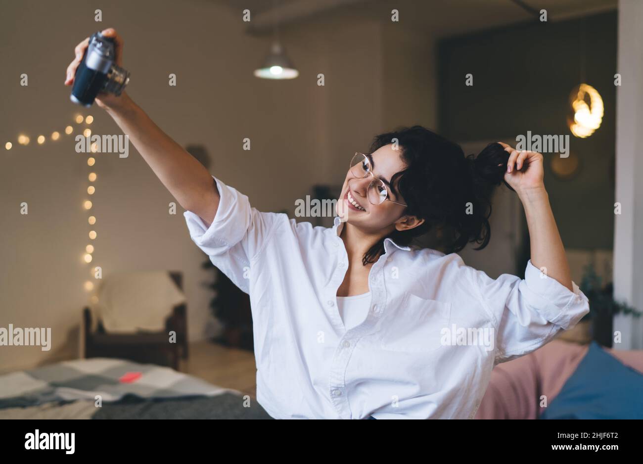Delighted woman taking selfie on vintage camera in blurred room Stock Photo