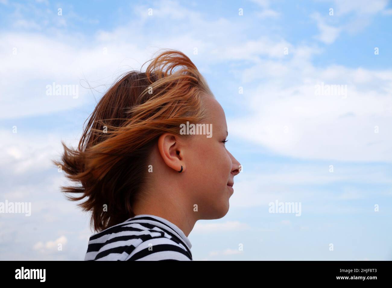 profile of a smiling red-haired teenage girl against a cloudy sky. Stock Photo