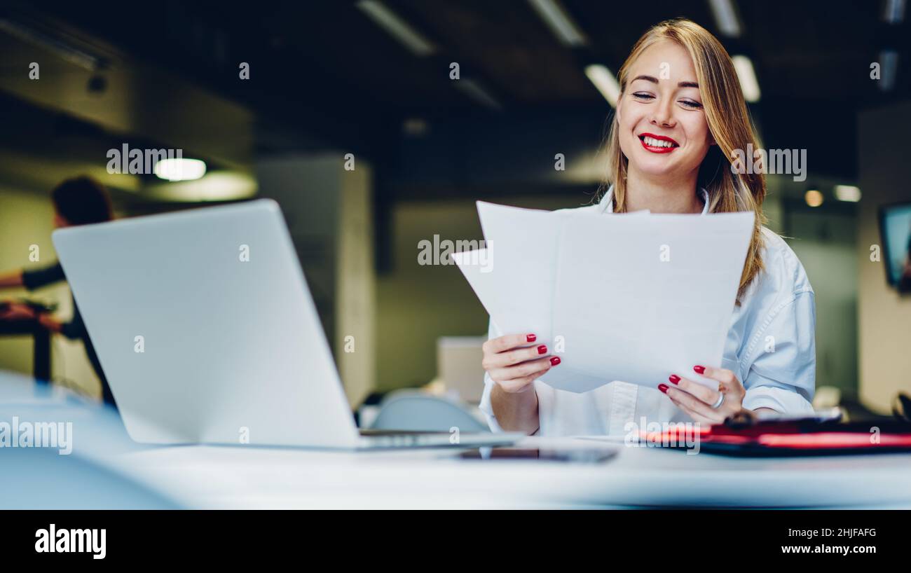 Positive female freelancer working with documents and laptop Stock Photo