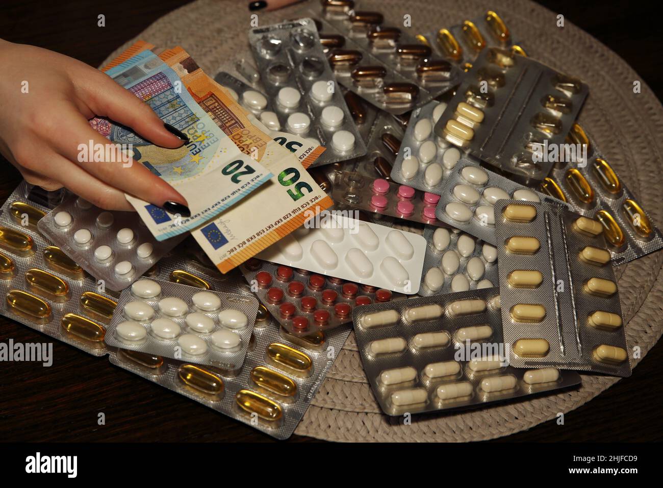 Female hand holds euro banknotes over many blisters of tablets, drugs, pills at the table Stock Photo