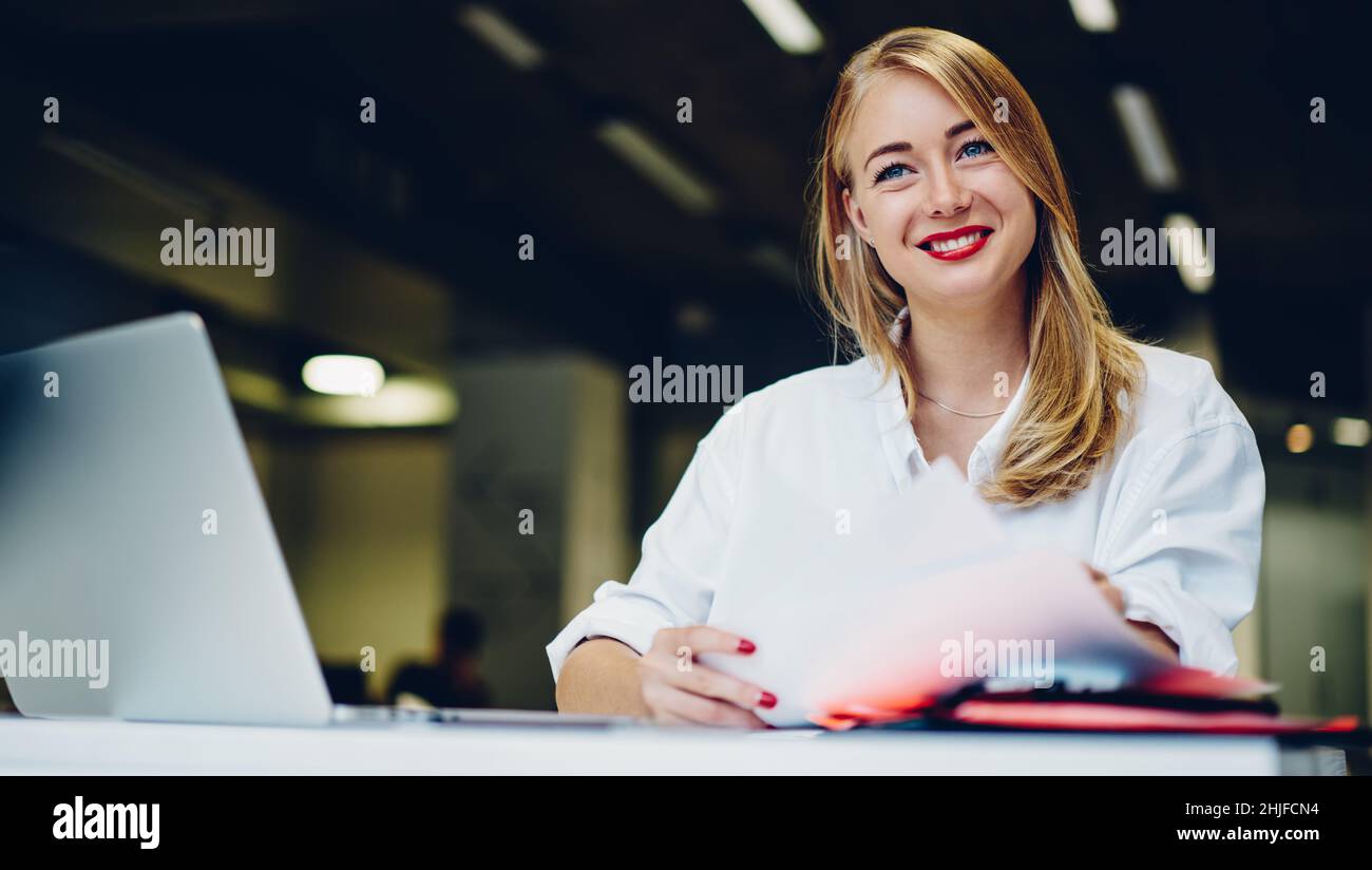 Smiling lady working remotely in cafe with laptop and papers Stock Photo