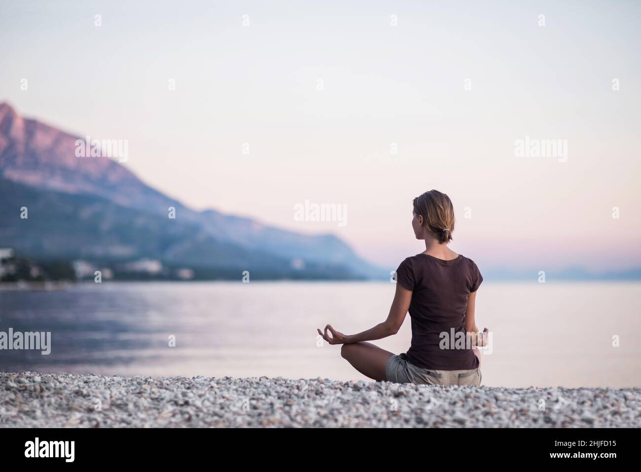 Young woman practicing yoga by the sea. Self care, breathing exercises, mindfulness, healthy lifestyle, relaxation, yoga and meditation concept Stock Photo