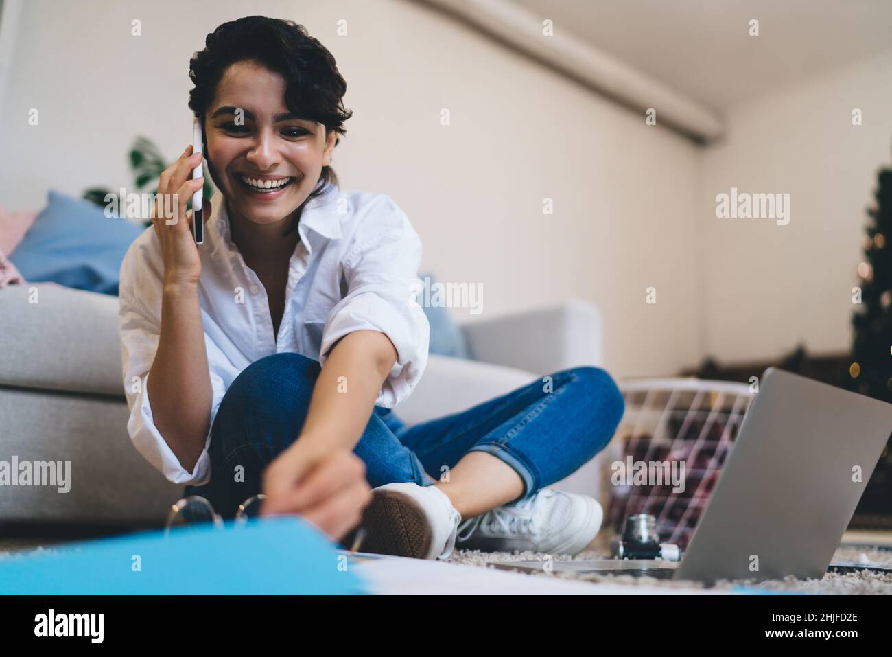 Positive young woman talking on smartphone during work online Stock Photo
