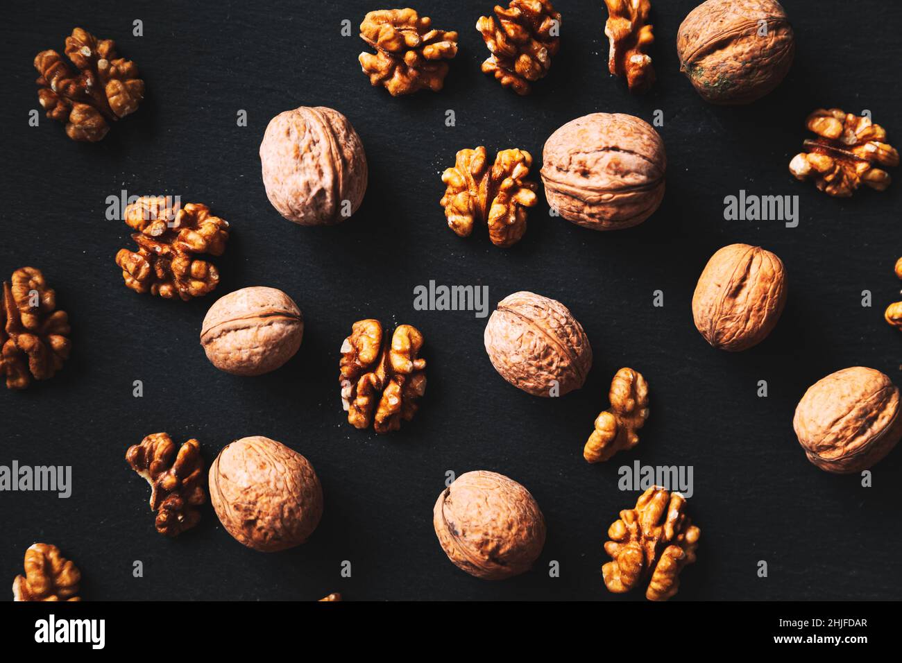Whole and peeled walnuts on a black background. Close-up, flat lay, top view. Food background, selective focus. Stock Photo