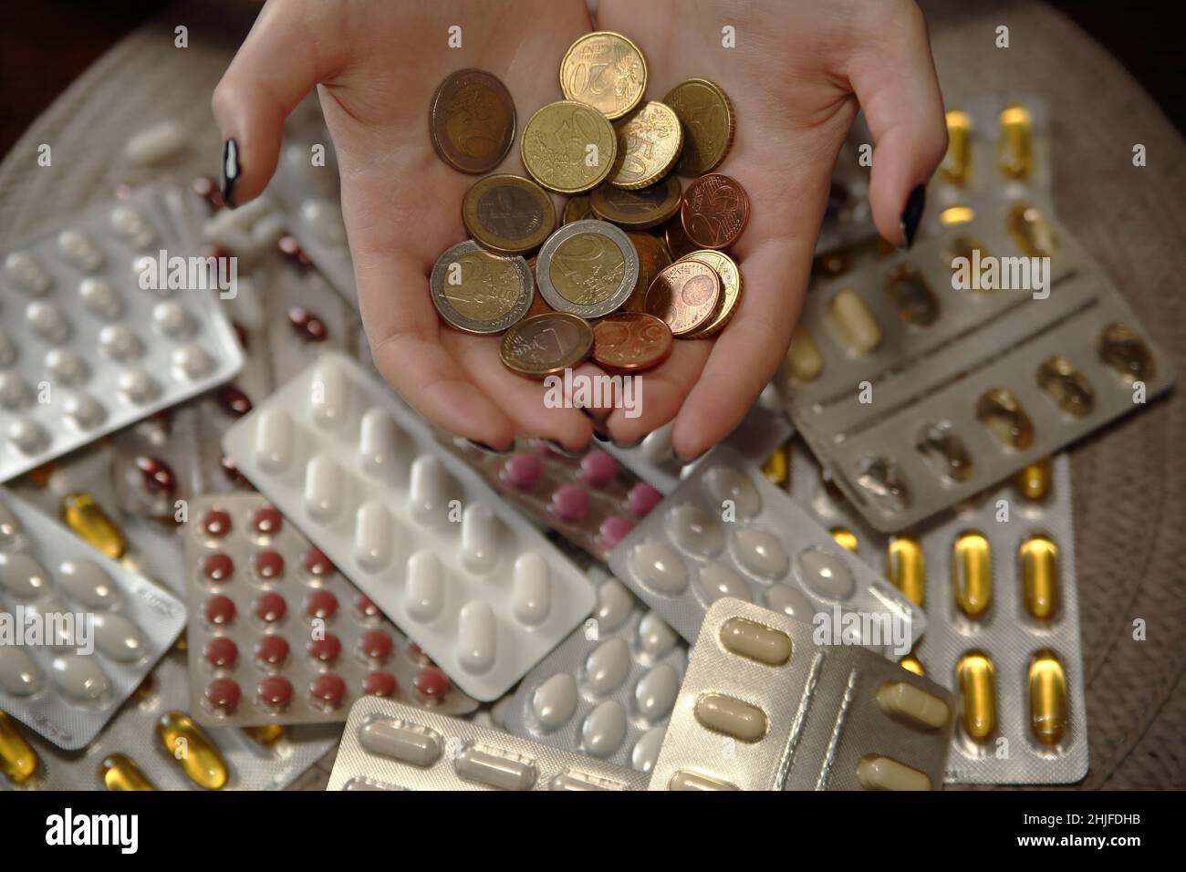 Euro coins in female hands over many blisters of pills, drugs, tablets and capsules Stock Photo