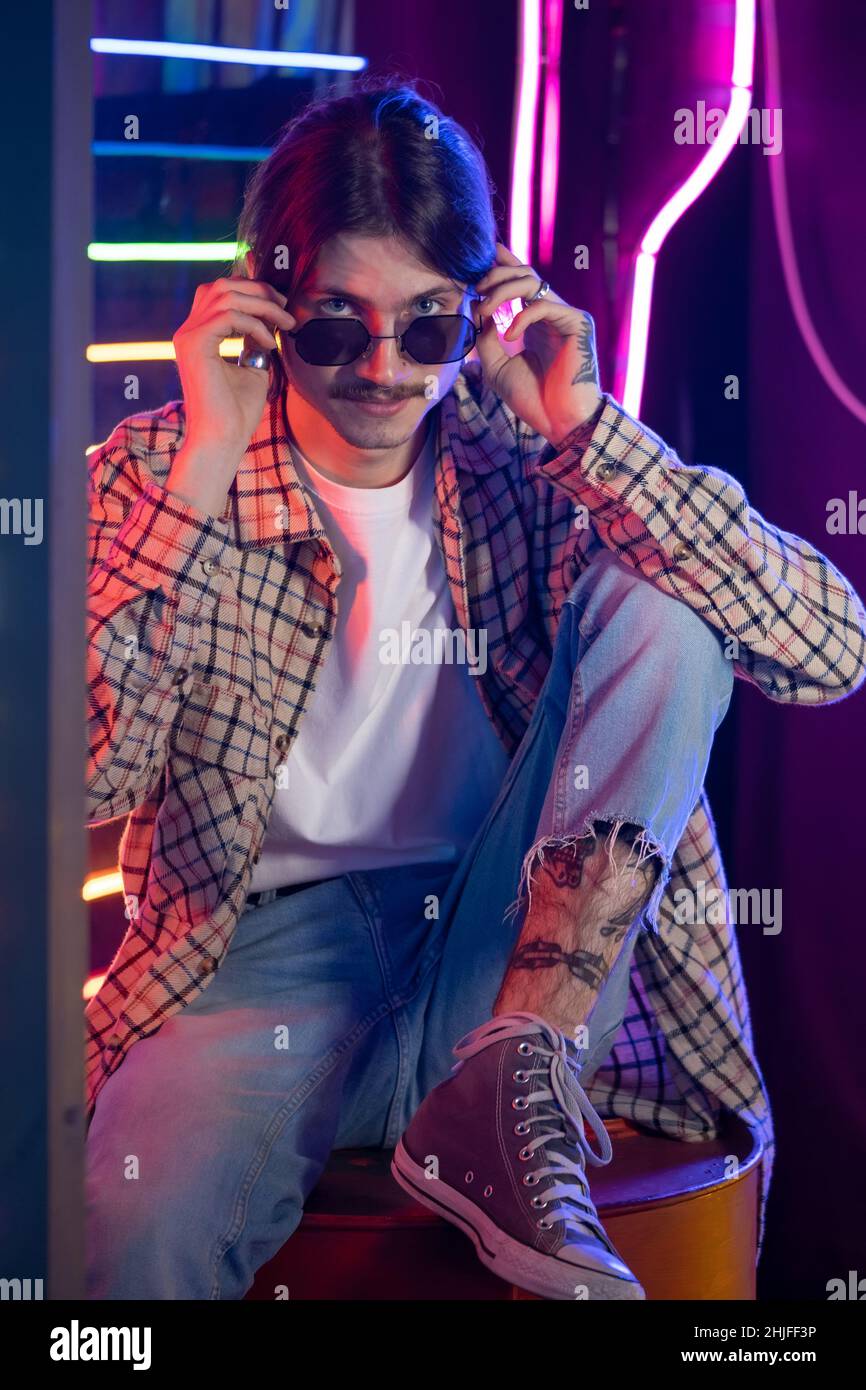 Millennial man in sunglasses and retro style enjoying nightclub atmosphere. Close-up portrait. Nostalgia and neon light interior Stock Photo