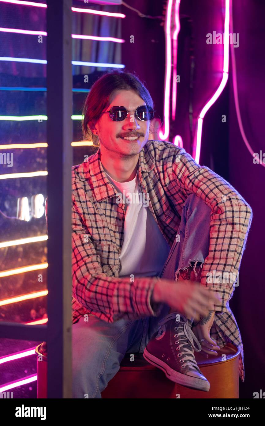 Millennial man in sunglasses and retro style enjoying nightclub atmosphere. Close-up portrait. Nostalgia and neon light interior Stock Photo