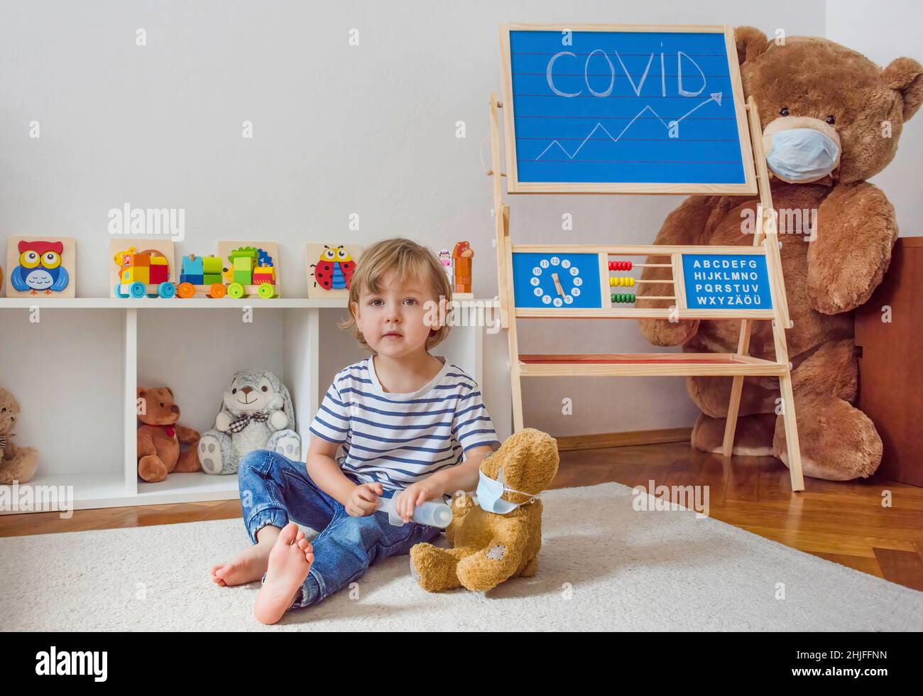 Cute child boy in home quarantine playing doctor on the floor with his sick teddy bears wearing medical masks during coronavirus COVID-2019 outbreak Stock Photo
