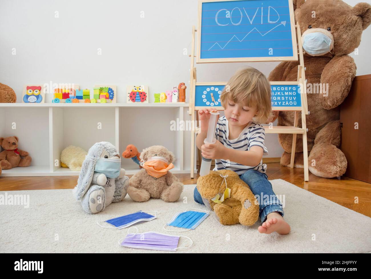Cute child boy in home quarantine playing doctor on the floor with his sick teddy bears wearing medical masks during coronavirus COVID-2019 outbreak Stock Photo