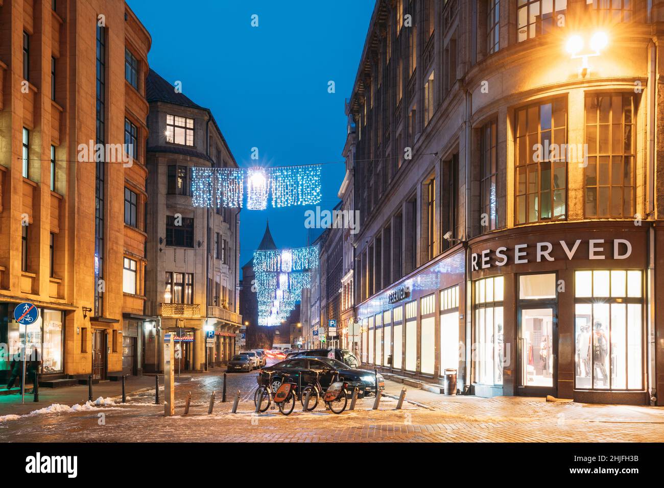 Riga, Latvia. Row Of Bicycles For Rent At Bike Parking Near Clothing Shop  The Reserved On Valnu Street In Lighting In Night Illumination. Reserved Is  Stock Photo - Alamy