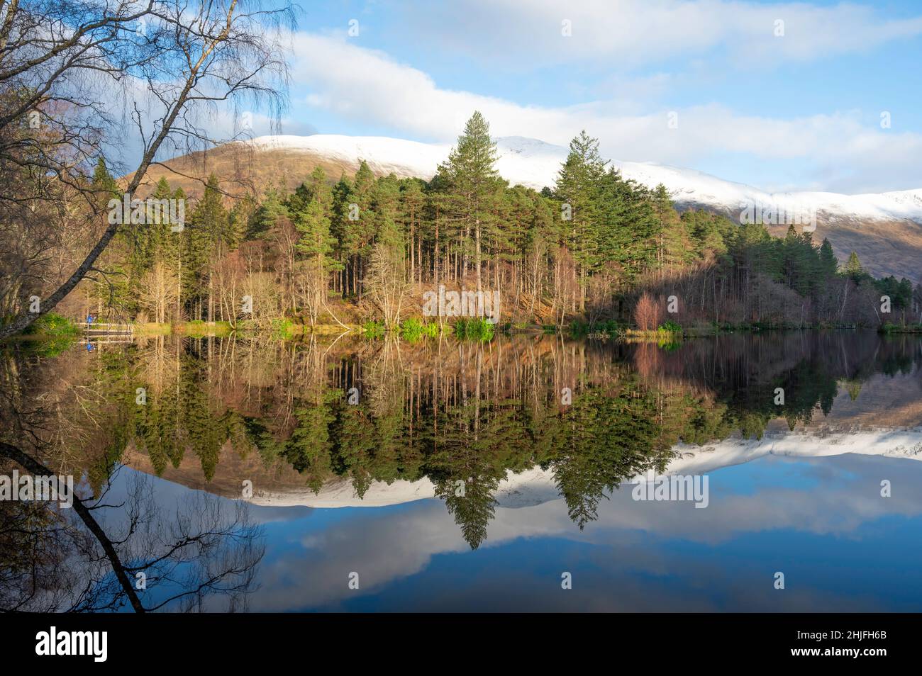 Glencoe lochan in Scottish Highlands in winter. Mirror reflection of trees, blue sky and forest in water. No people. Stock Photo