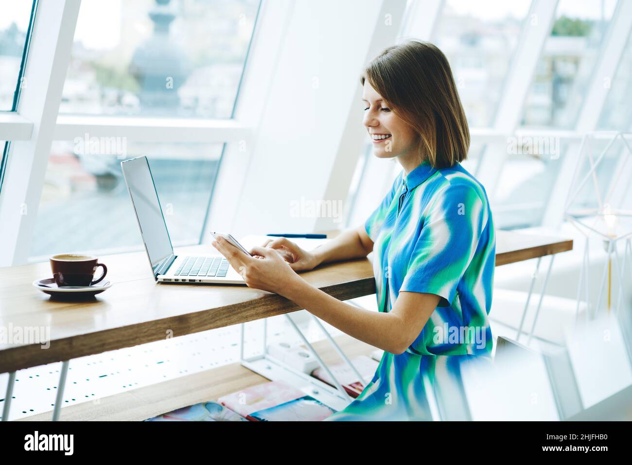 Smiling female freelancer browsing smartphone in light workplace Stock Photo