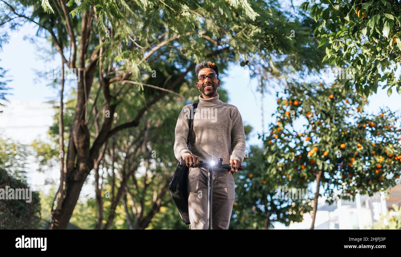 Afro-american man with turtleneck vest enjoying a ride with his electric scooter towards camera Stock Photo