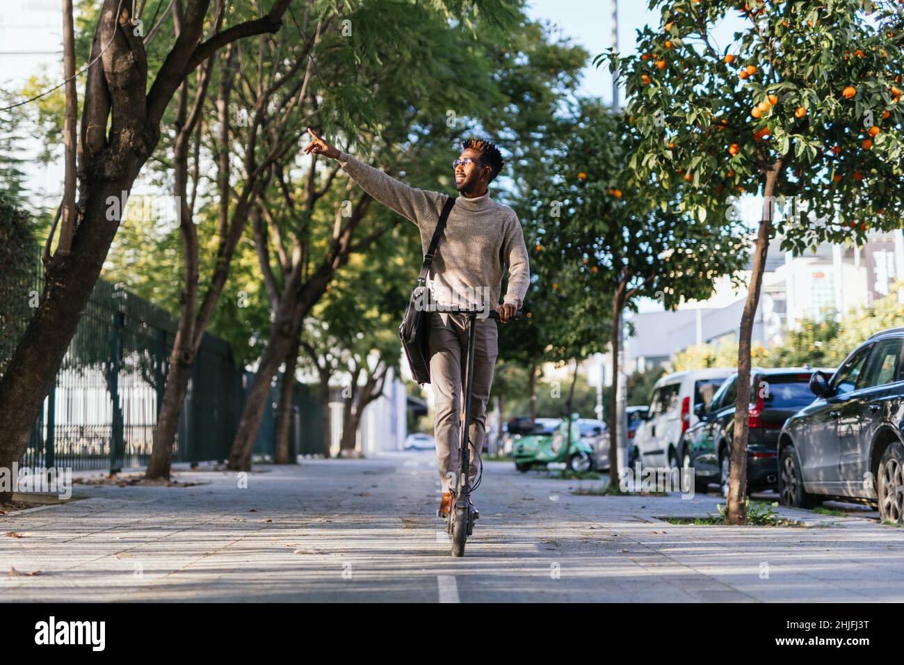 African-american man with turtleneck vest enjoying a ride with his electric scooter and pointing with his arm Stock Photo