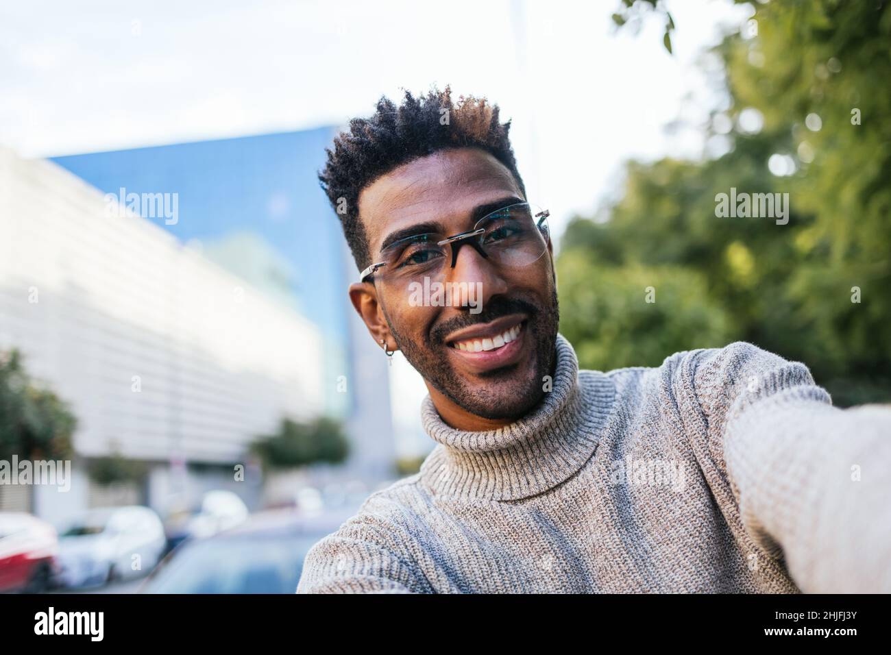 African American man in turtleneck vest and glasses taking a selfie in the city Stock Photo