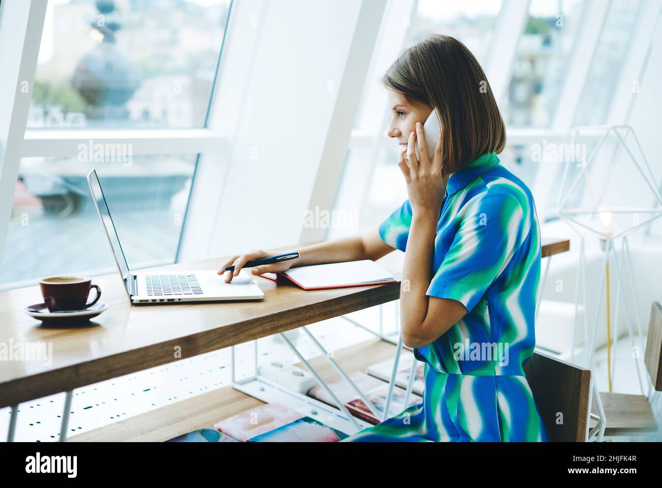 Smiling female student talking on smartphone in modern workplace Stock Photo