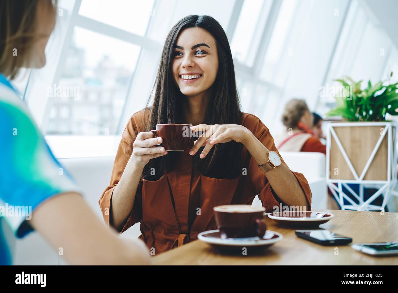 Happy woman with cup of coffee and friend in cafe Stock Photo