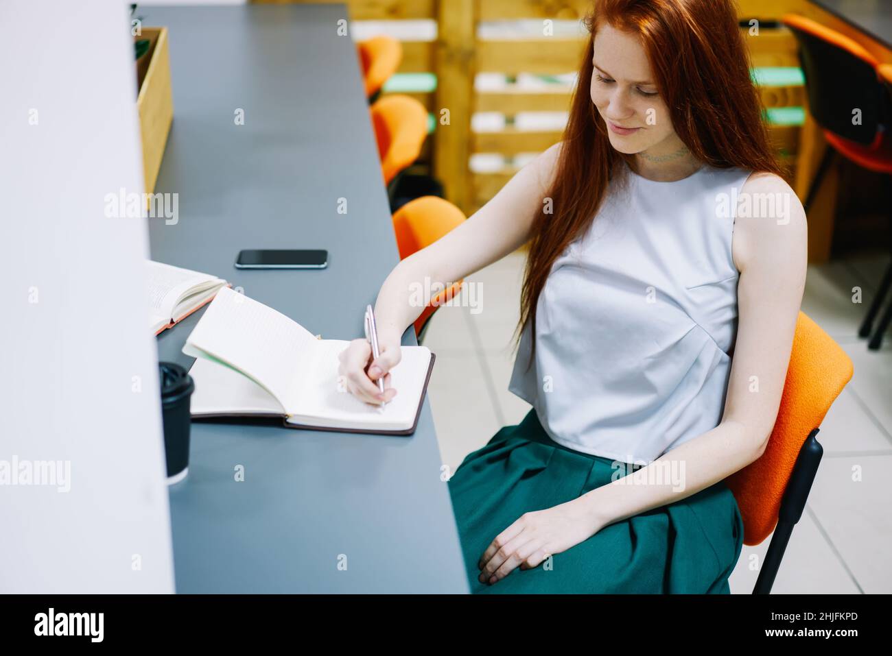 Young lady writing notes while sitting in chair Stock Photo