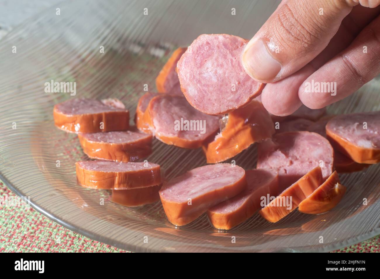 Calabresa sausage sliced on a plate with hand holding a slice,simple concept of cold cuts,Brazilian calabresa. Stock Photo