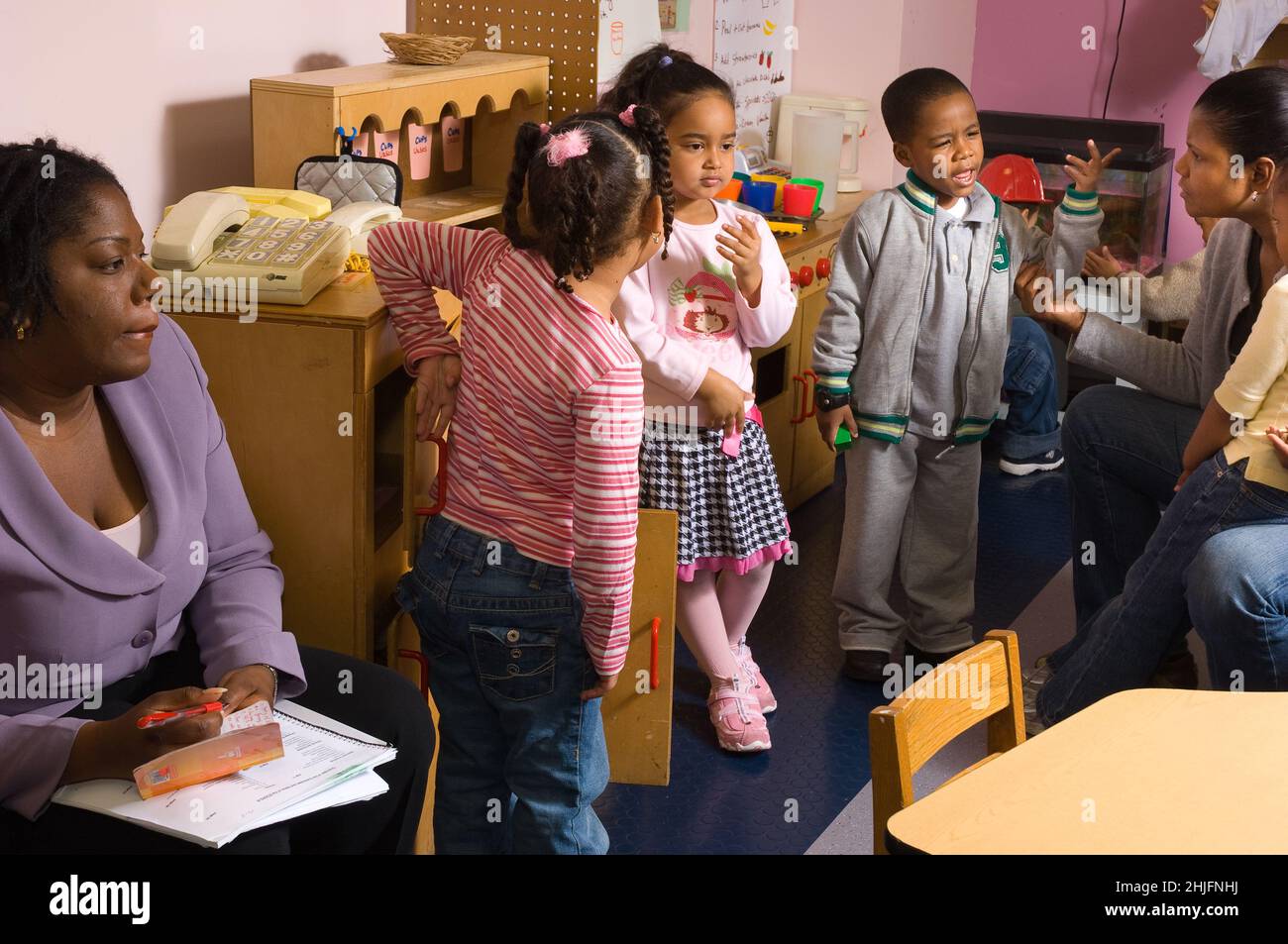 Education Preschool classroom ages 4-5 observer watches as female teacher works with two children to resolve dispute, two other children waiting to st Stock Photo