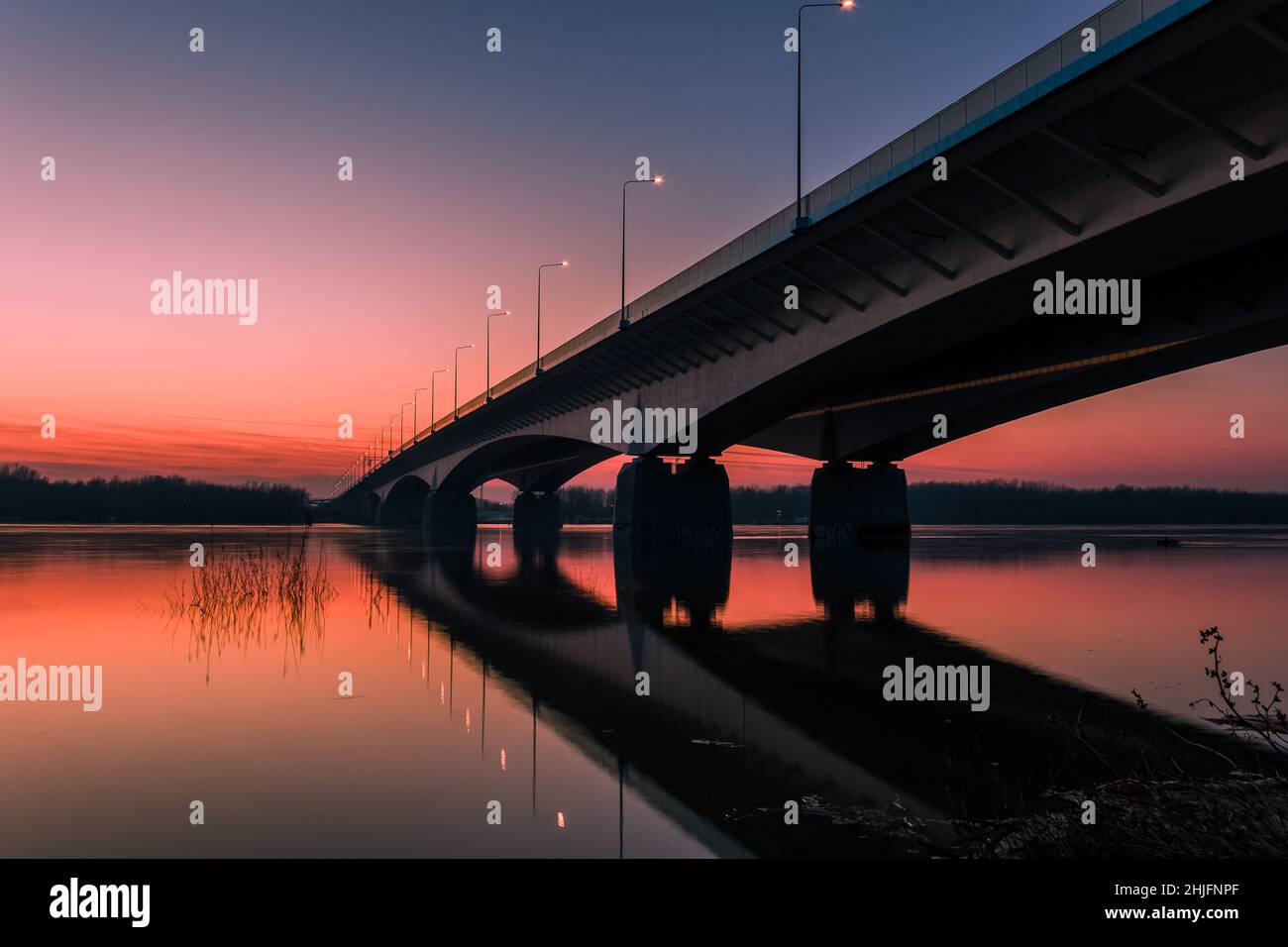 Colorful Warsaw bridge across Vistula River with reflections in water at sunset. Stock Photo