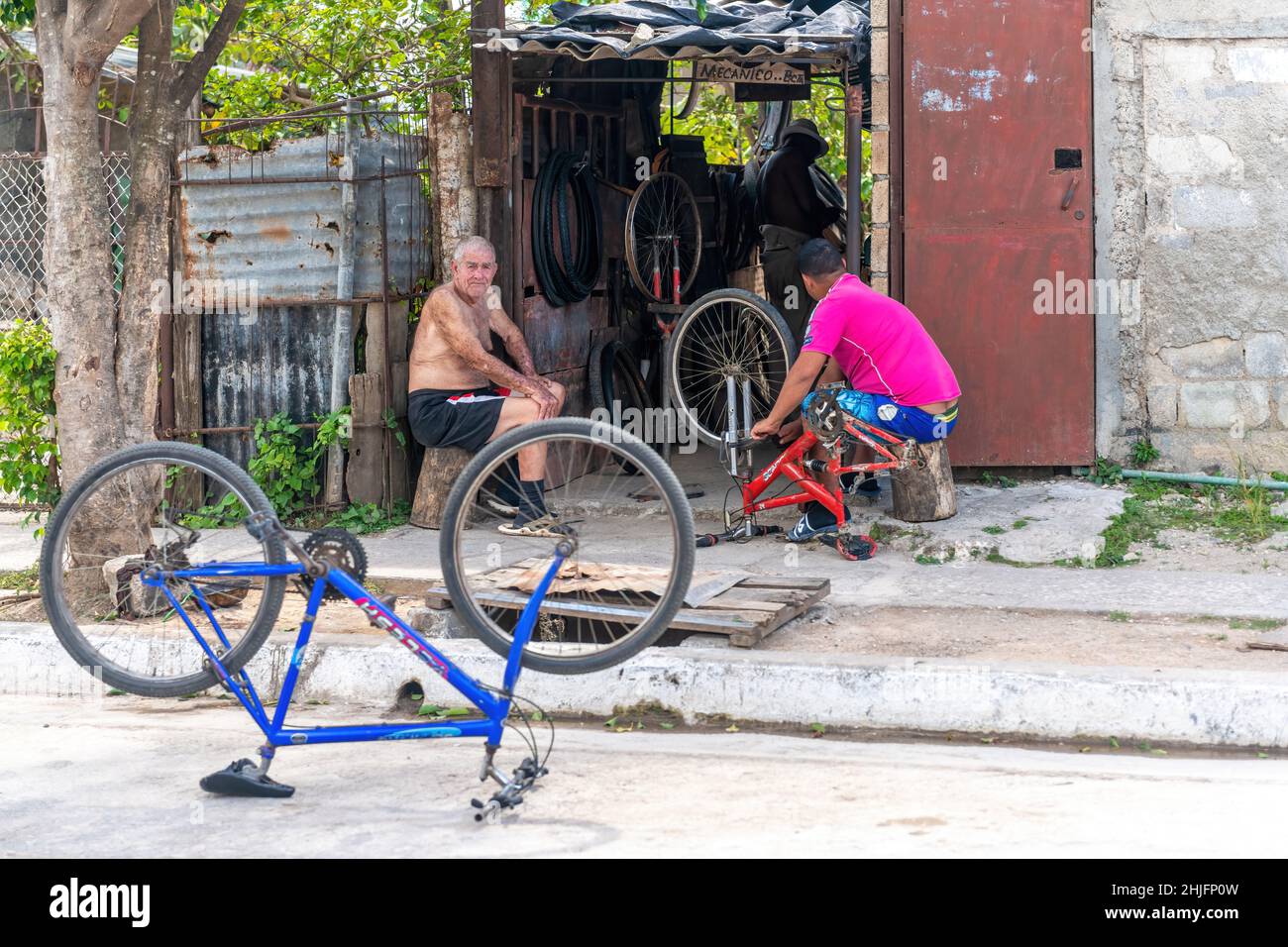 A bicycle repair shop in the La Vigia neighborhood. Two men sit at the door of the run-down building. Stock Photo