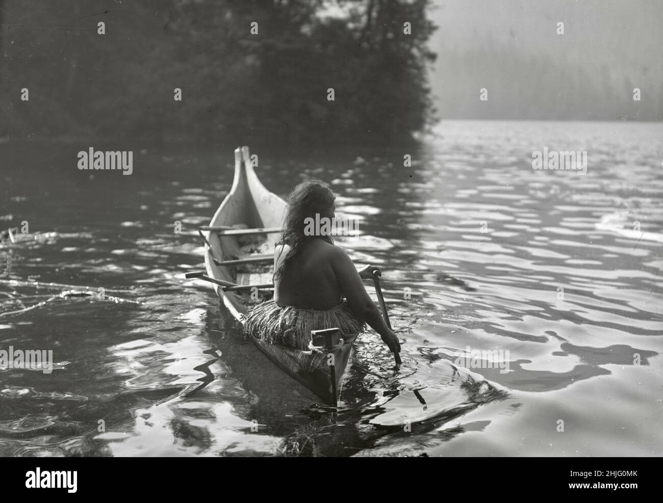 Edward S Curtis photograph - Clayoquot Indian paddling canoe into area shaded by trees - 1910 Stock Photo