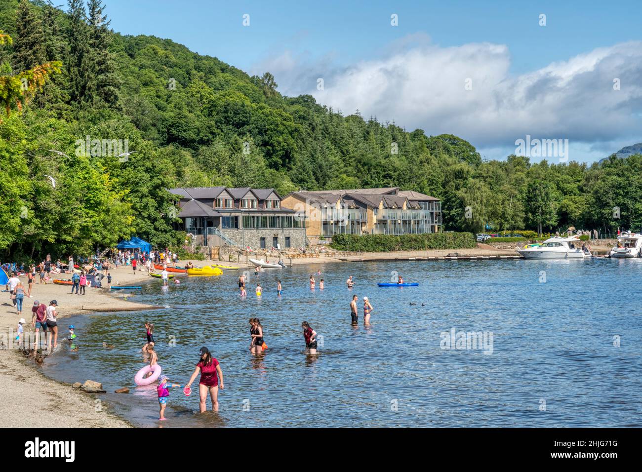 People on beach at Luss beside Loch Lomond. With Lodge on Loch Lomond hotel in background. Stock Photo