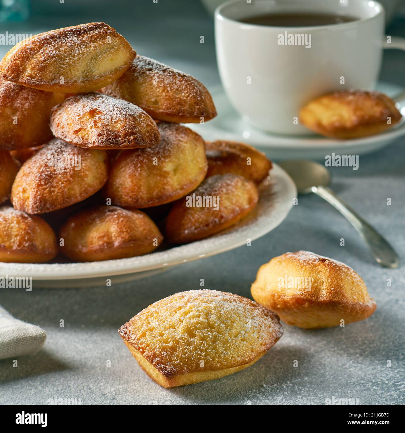 Heap of madeleine cookies on dish and tea on gray background Stock Photo