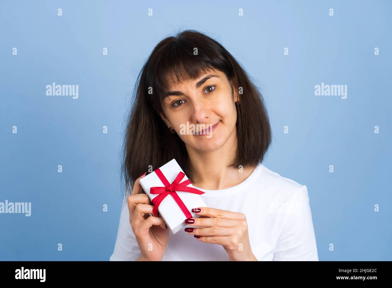 Smiling happy woman holding gift box isolated on blue background. Valentines day or birthday concept Stock Photo