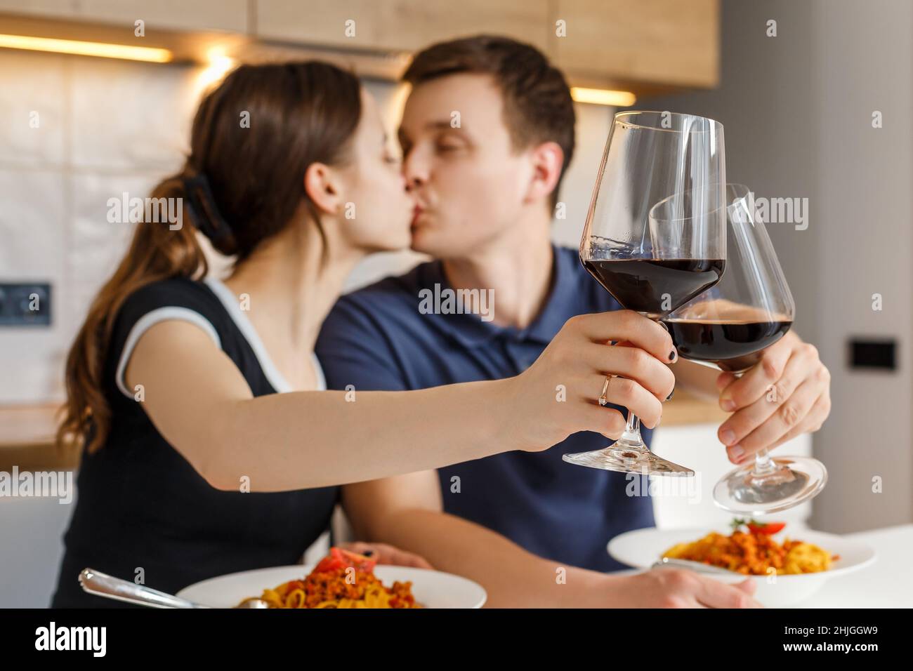 Romantic dinner at home. Happy couple kissing, clinking glasses and