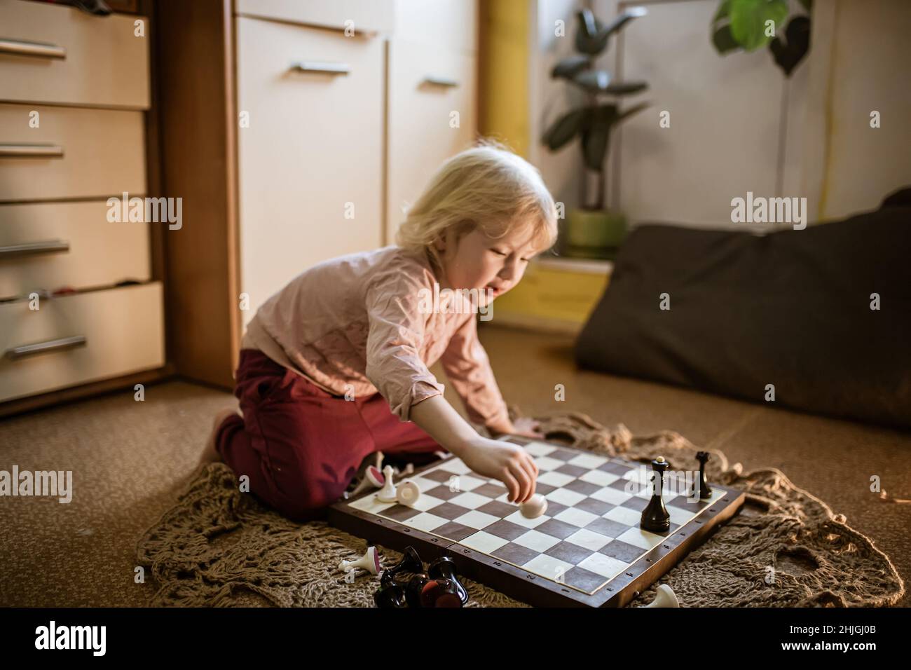 child plays single game of chess at home on floor. Chessboard with the end of the game of chess