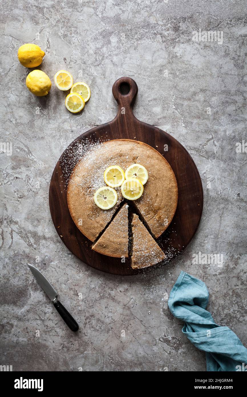 A sliced lemon cake on a wood cutting board with fresh lemons Stock Photo