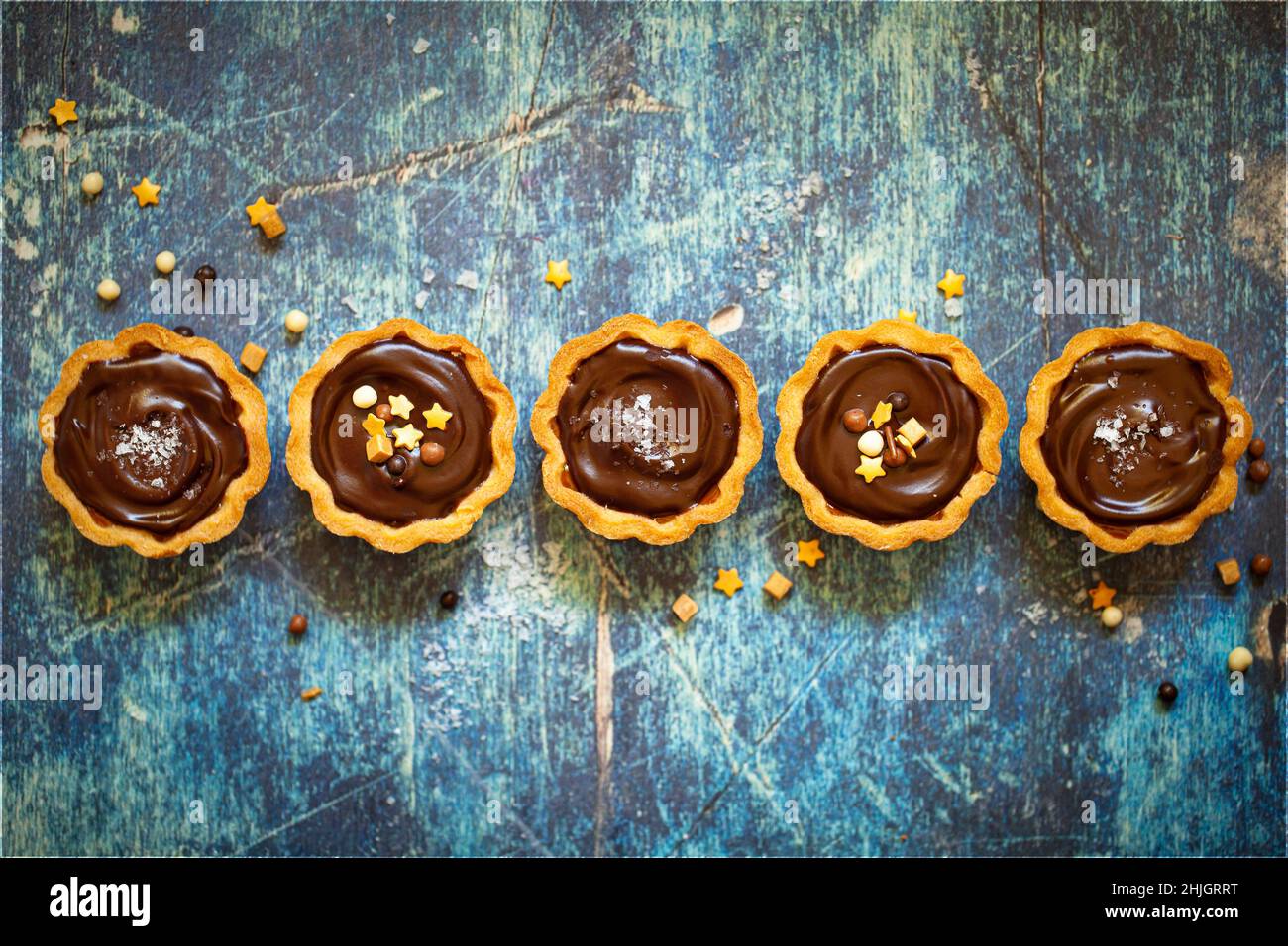 A row of chocolate caramel tarts topped with sprinkles and sea salt