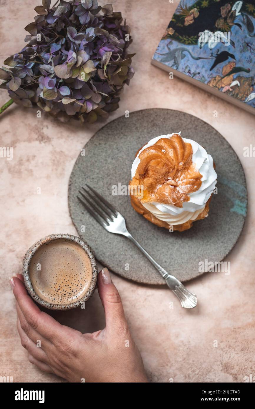 Woman drinking coffee and eating cream puff dessert served on a ceramic dessert plate Stock Photo