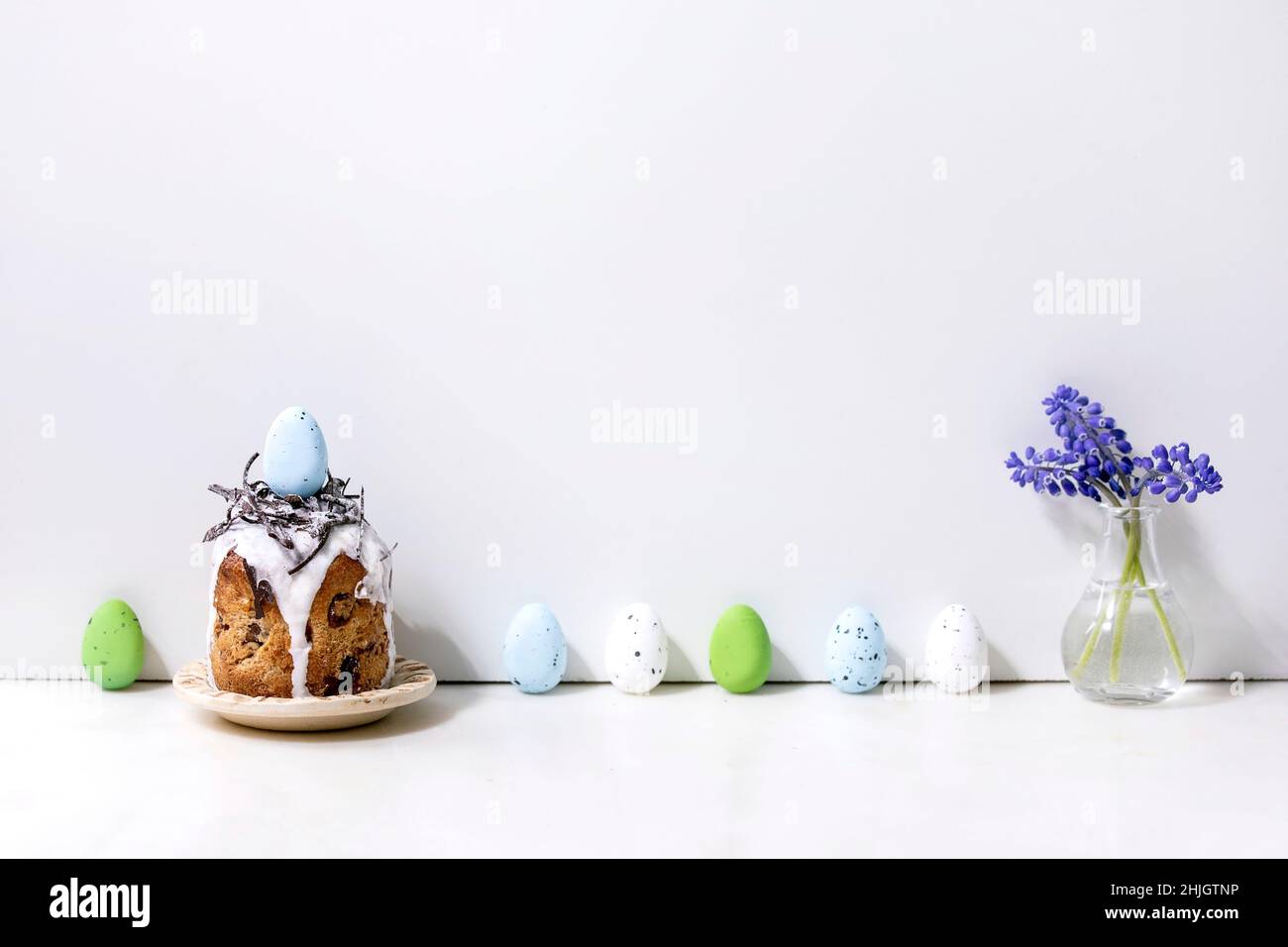 Homemade traditionla Easter kulich cake with chocolate nest and eggs on plate standing on white marble table with colored eggs in row. Traditional ort Stock Photo