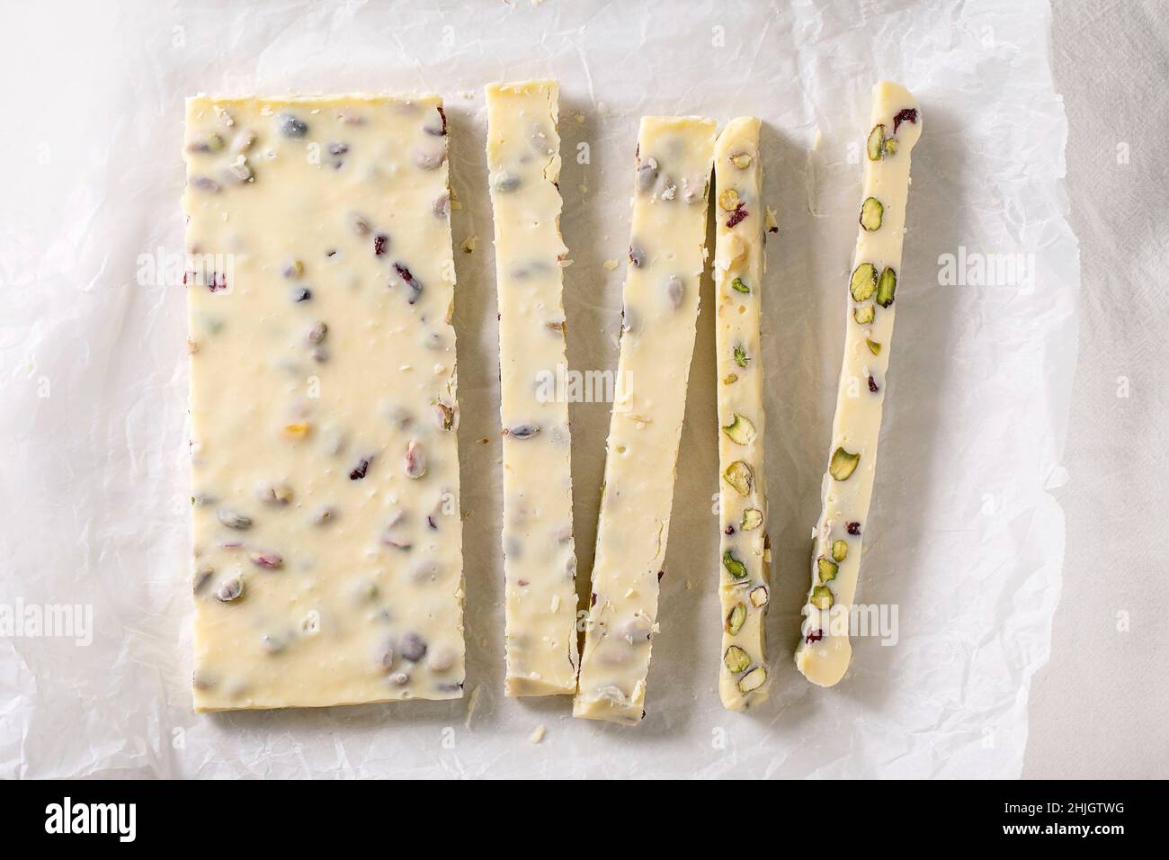 Sliced homemade white chocolate candy bar with pistachios nuts and cranberries on crumpled paper. Handmade food sweet gifts for any holidays. Stock Photo