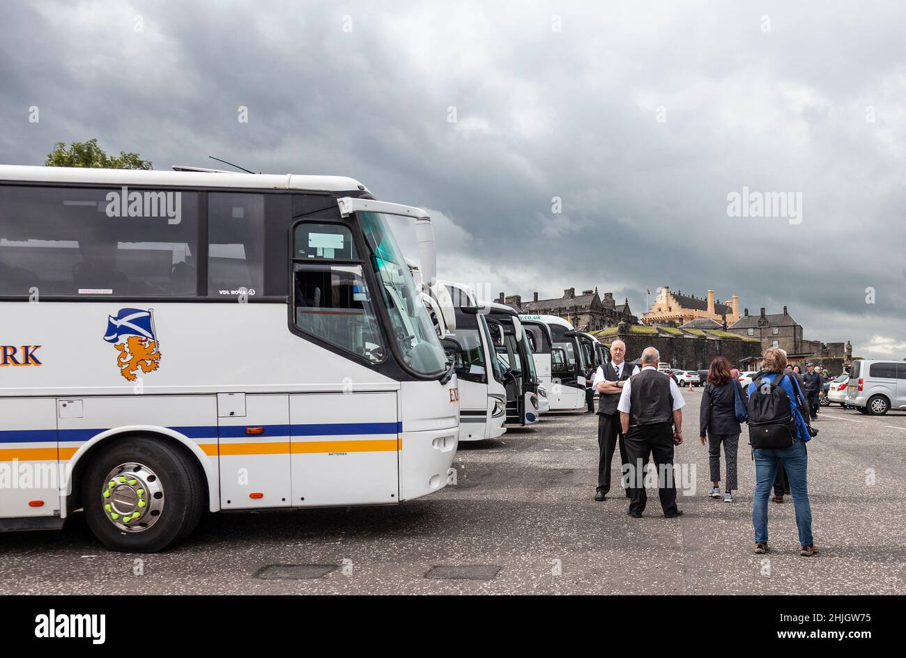 Coaches lines up in the esplanade of Stirling Castle, in Stirling, Scotland. Coach drivers chat while visitors to the castle pass by. Stock Photo