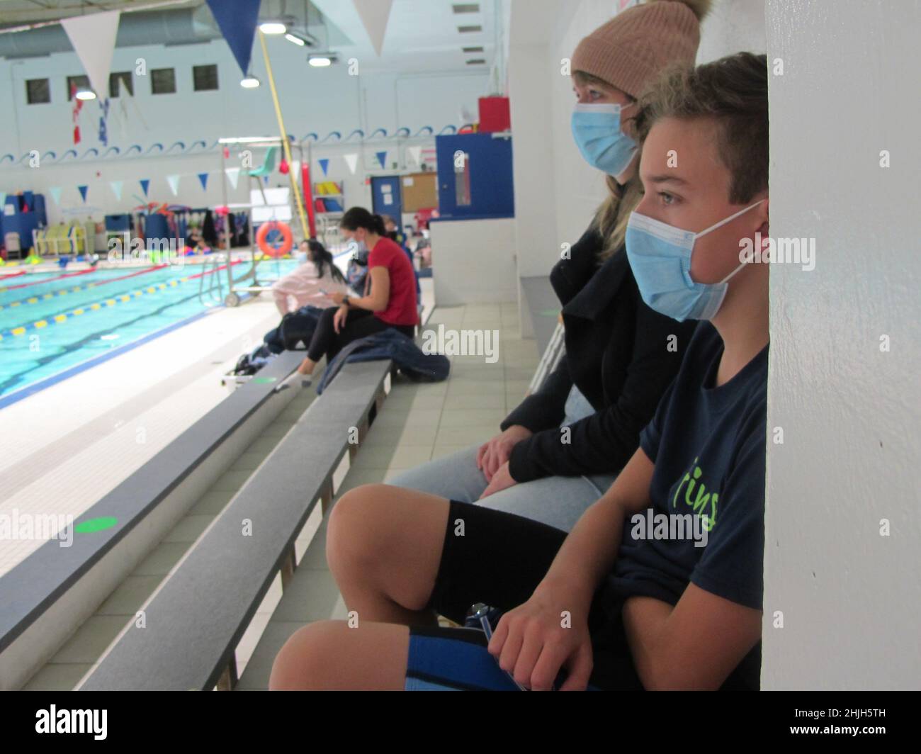 Woman and boy watching swimmers while wearing masks during Covid Stock Photo