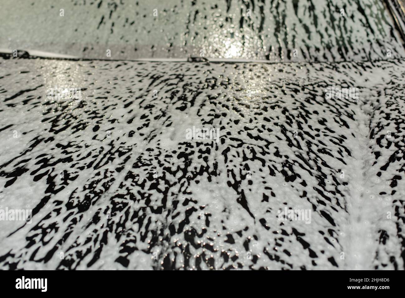 Soap foam on car. Texture of white foam on black car. Washing of transport. Washing agent on surface. Stock Photo