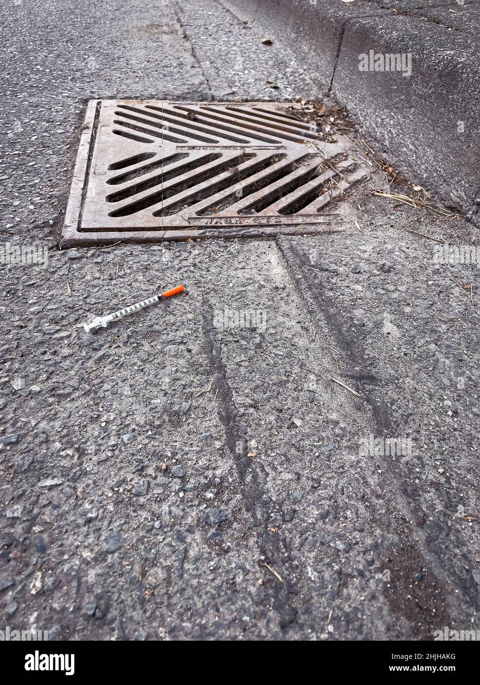Syringe beside storm drain. Stock Photo