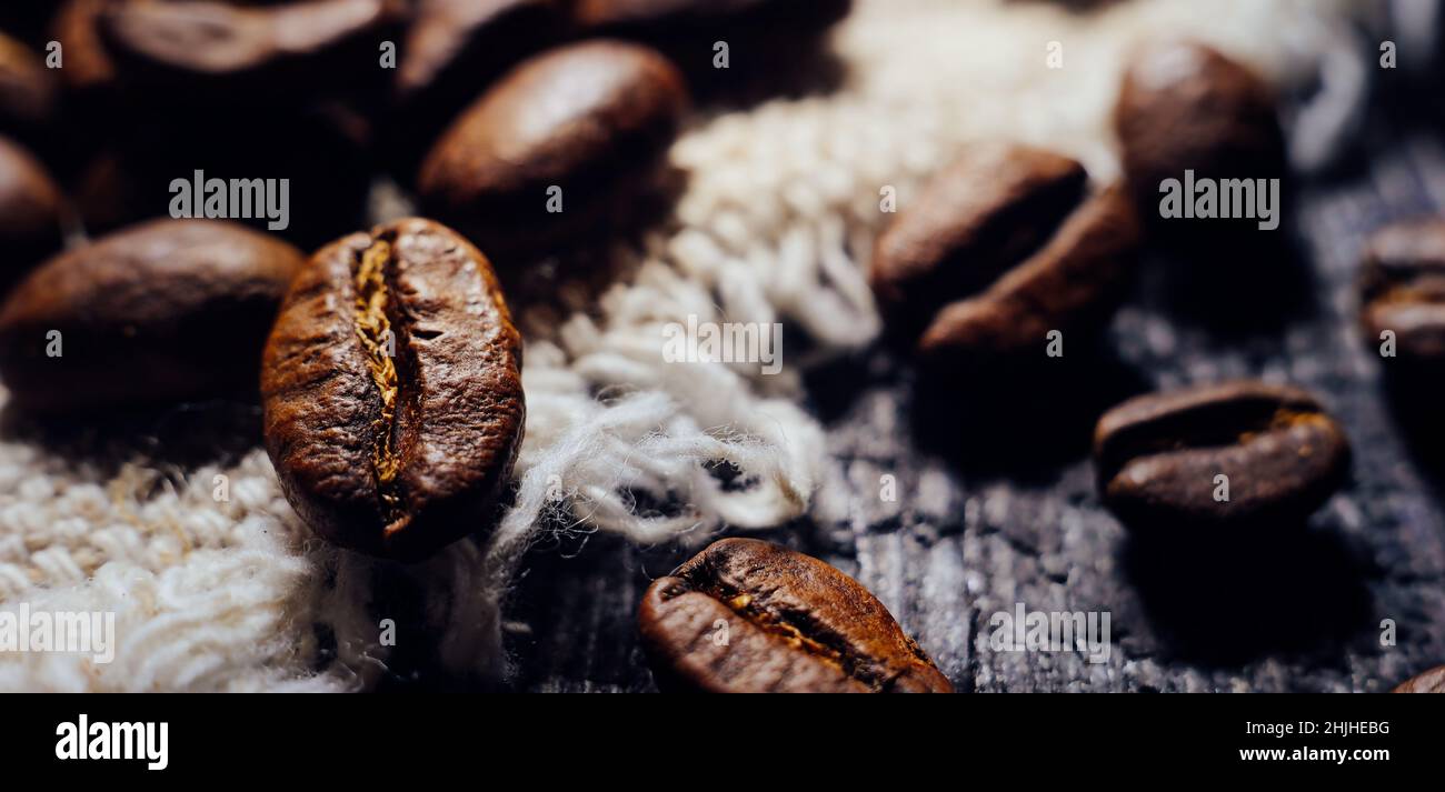 Macrophotography of coffee beans lie on textured wood and burlap. Fresh harvest aromatic coffee. Selective focusing. Back for cafe, restaurant or coffee shop. advertising banner Stock Photo